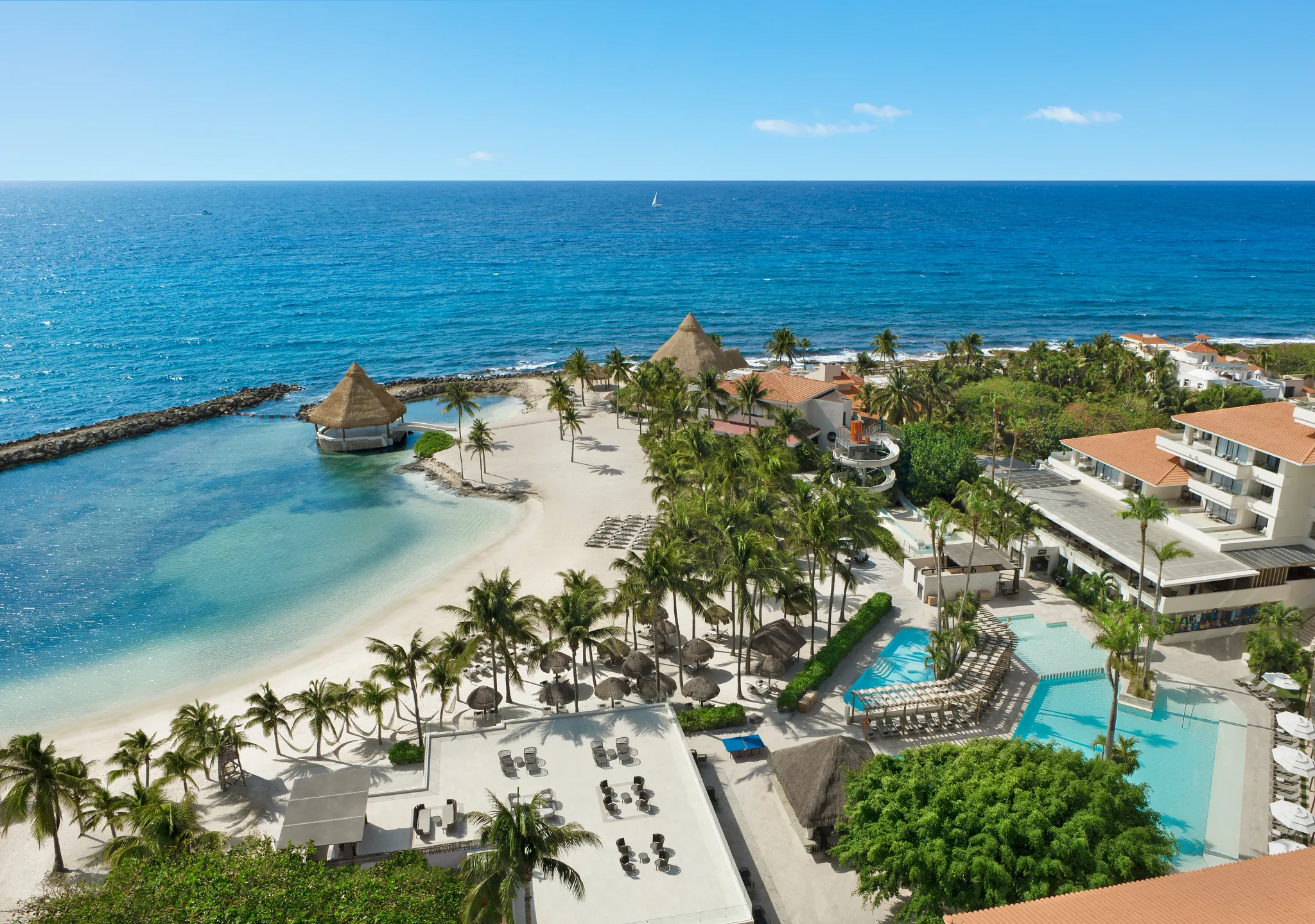 Aerial view of sandy beach with lounge chairs and calm lagoon waters at Dreams Aventuras Riviera Maya.