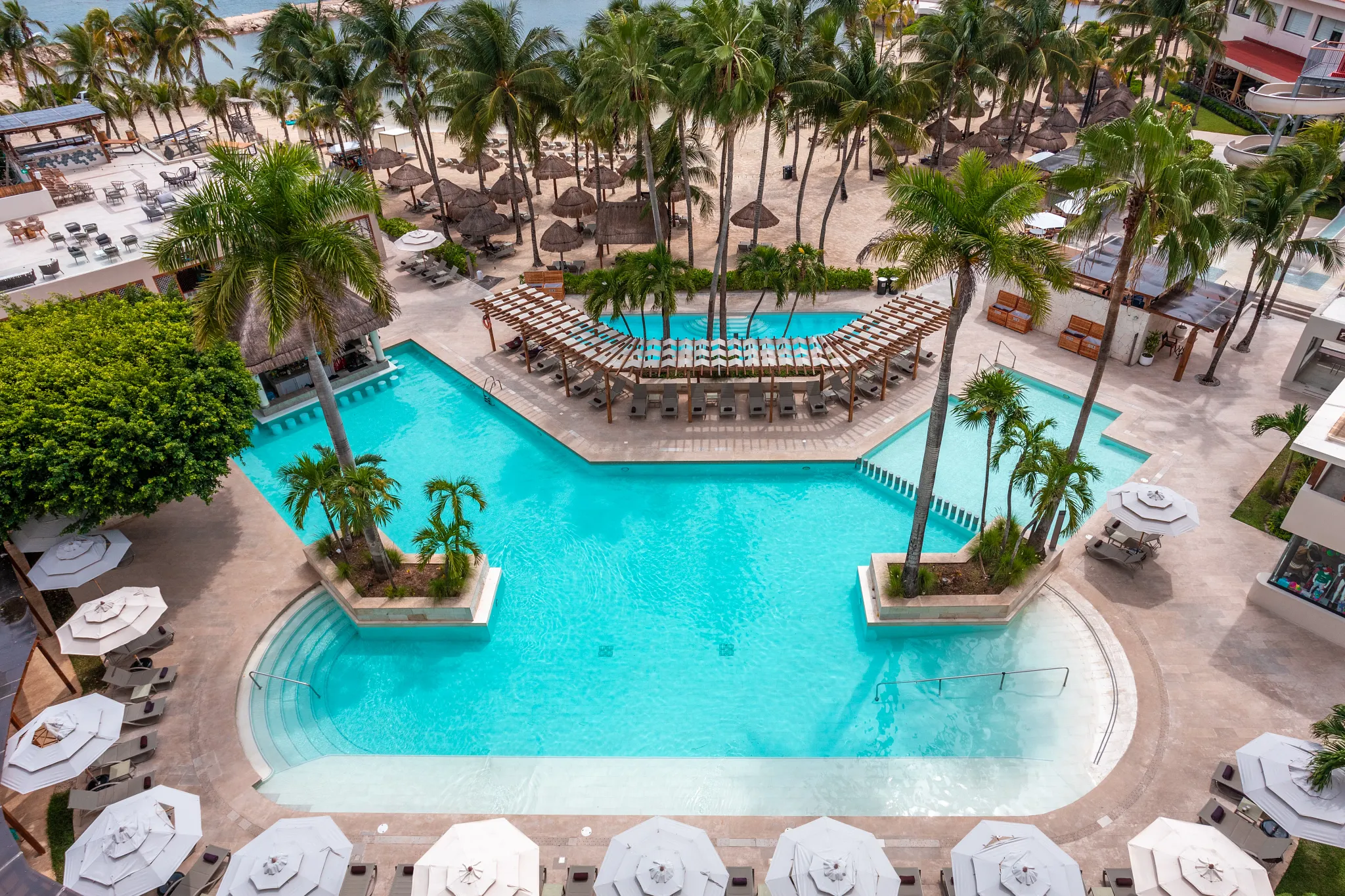 Aerial view of family pool with lounge chairs and palm trees at Dreams Aventuras Riviera Maya.