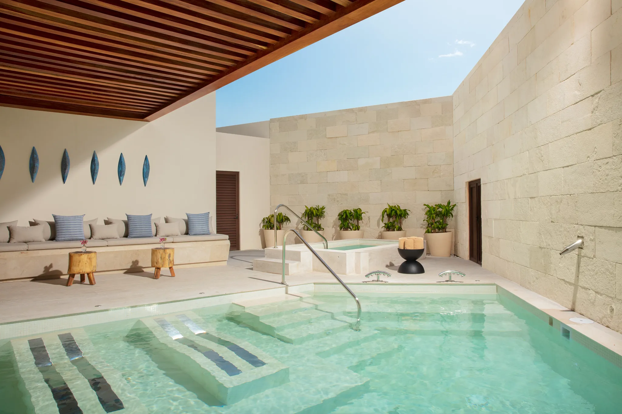 Outdoor hydrotherapy pool with loungers and stone walls at Dreams Aventuras Riviera Maya spa.