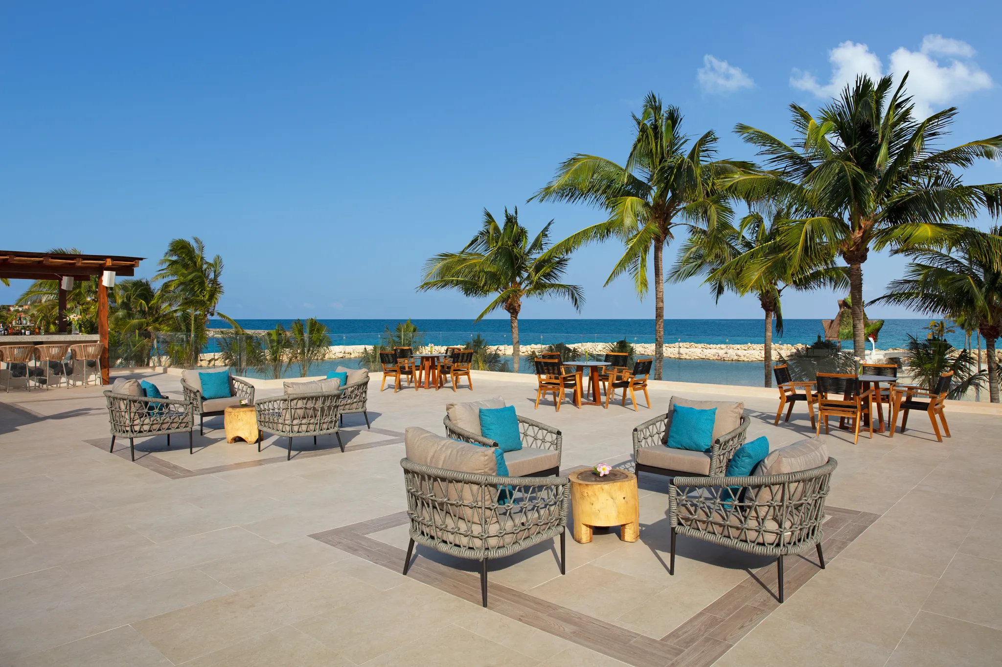 Oceanfront rooftop lounge with seating and palm trees overlooking the Caribbean Sea at Dreams Aventuras Riviera Maya.