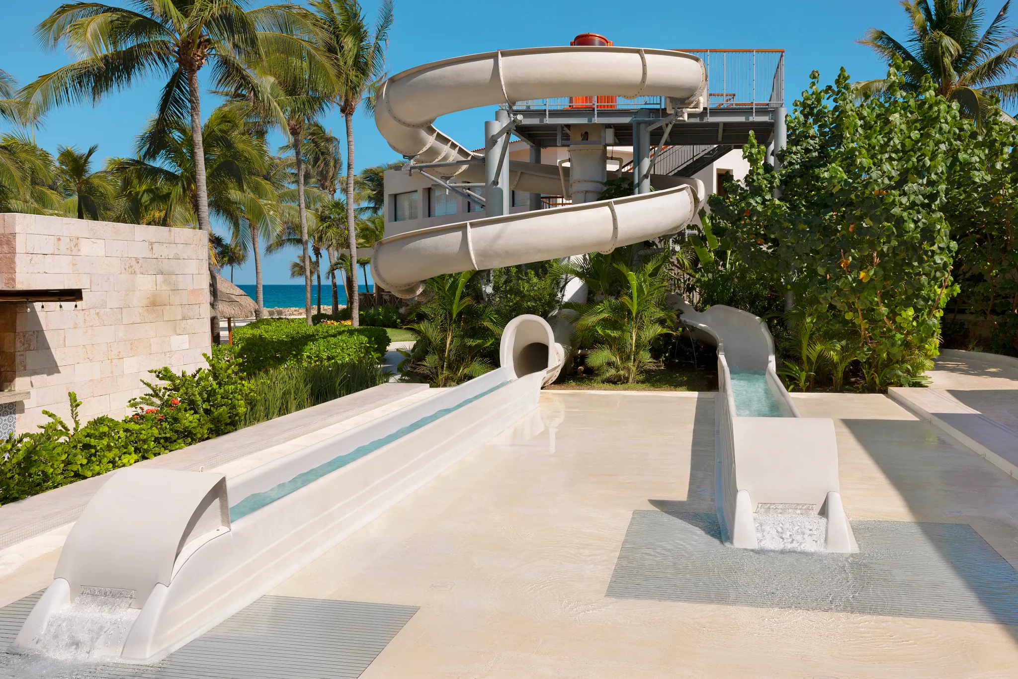 Resort water slides surrounded by palm trees near the beach at Dreams Aventuras Riviera Maya.